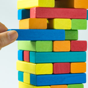 Hand pulling colorful wooden block from the tower in as Risk or stability concept.
